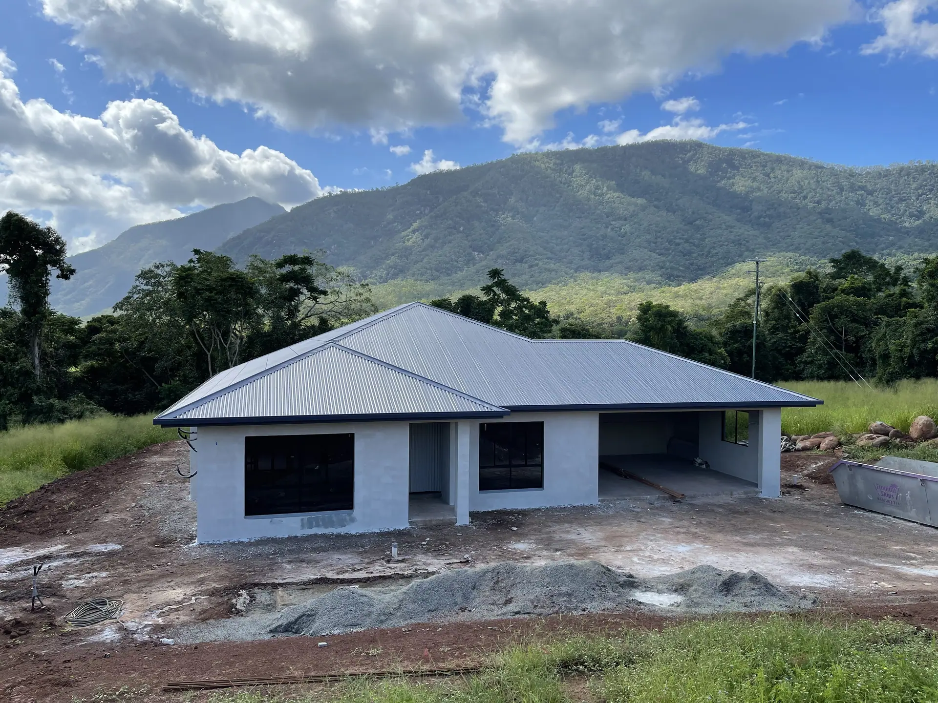 New home with a grey metal roof below rainforest-covered hills