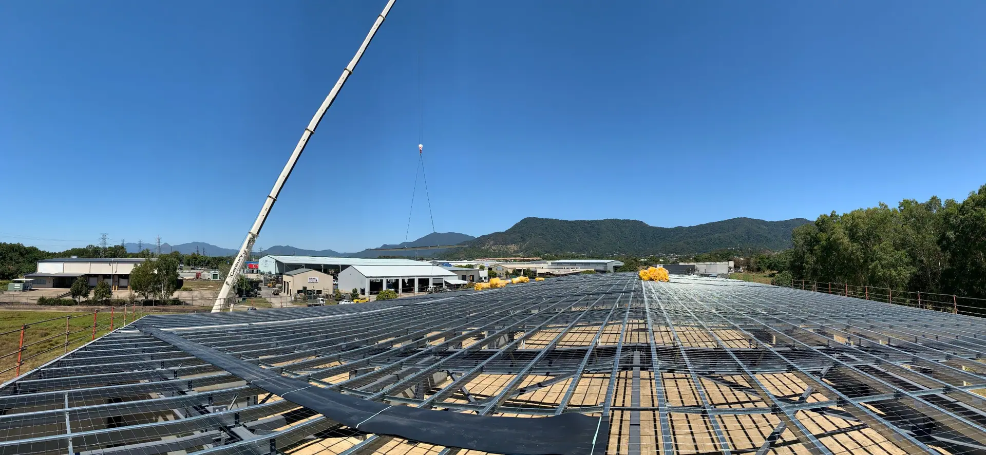 Steel roof framing and safety mesh on a large commercial build, with a crane and mountains behind